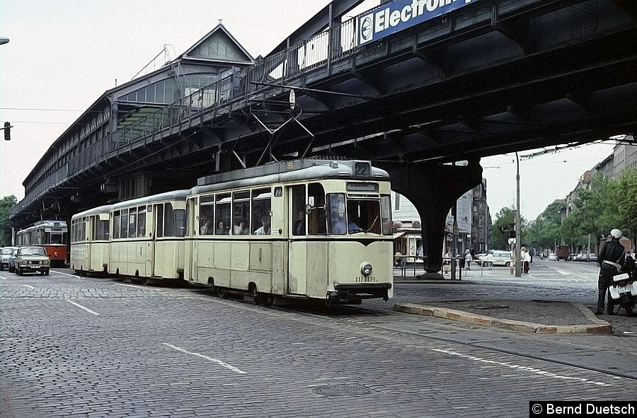 Bild: Unter dem Viadukt der U-Bahn-Linie 2 in der Schönhauser Allee fährt ein Dreiwagenzug der Linie 22 Richtung Innenstadt. 
Ihm folgt ein Dreiwagenzug der Linie 49. Die querenden Gleise wurden damals von der Linie 4 befahren. Anscheinend interessiert sich der im Bild rechts zu sehende VOPO ebenfalls für die Straßenbahn.